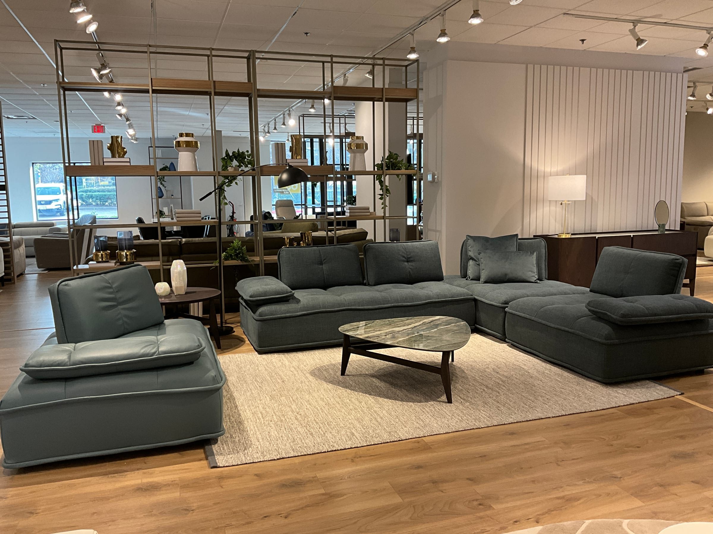 Modular sectional and armless chair grouping around an oval marble coffee table, backed by an open shelving room divider.