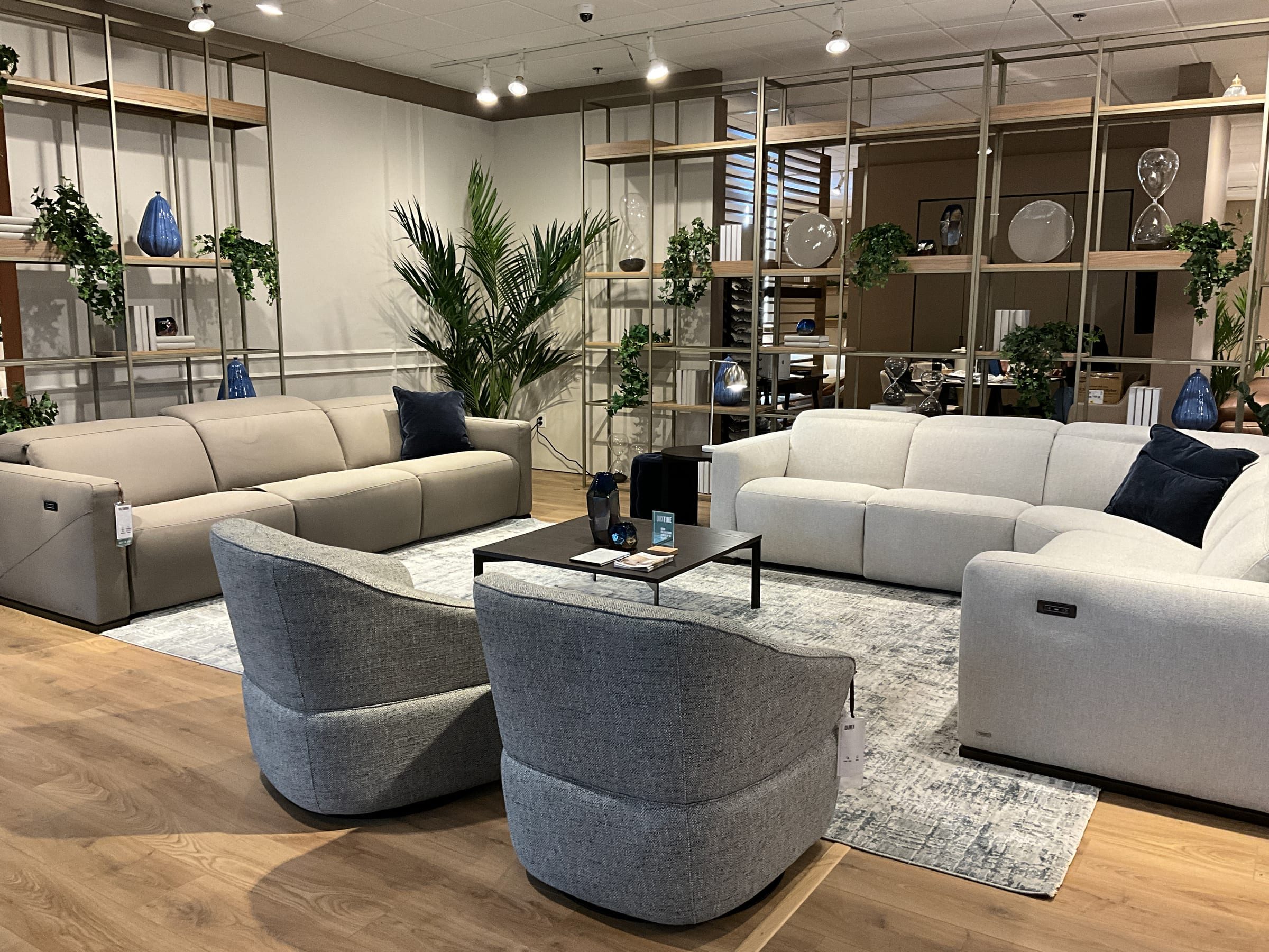 Two reclining sofas and swivel chairs staged around a glass-and-marble coffee table, backed by an open shelving divider.