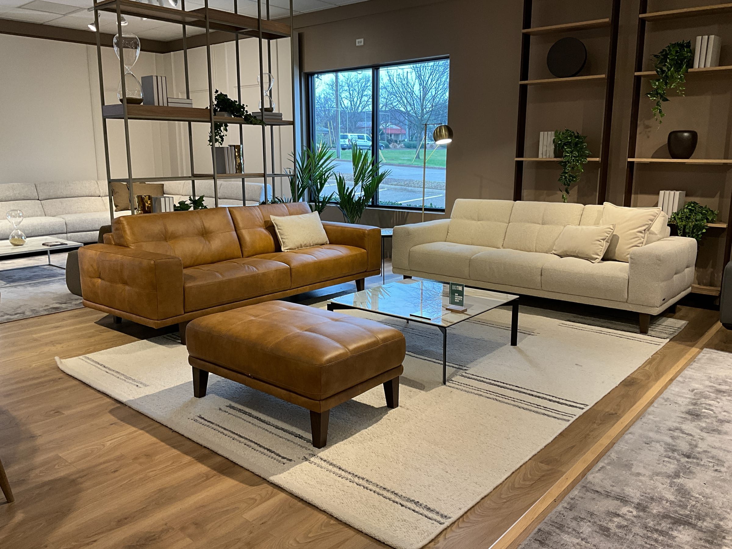 Cognac leather sofa and ottoman paired with a cream fabric sofa around a glass coffee table.