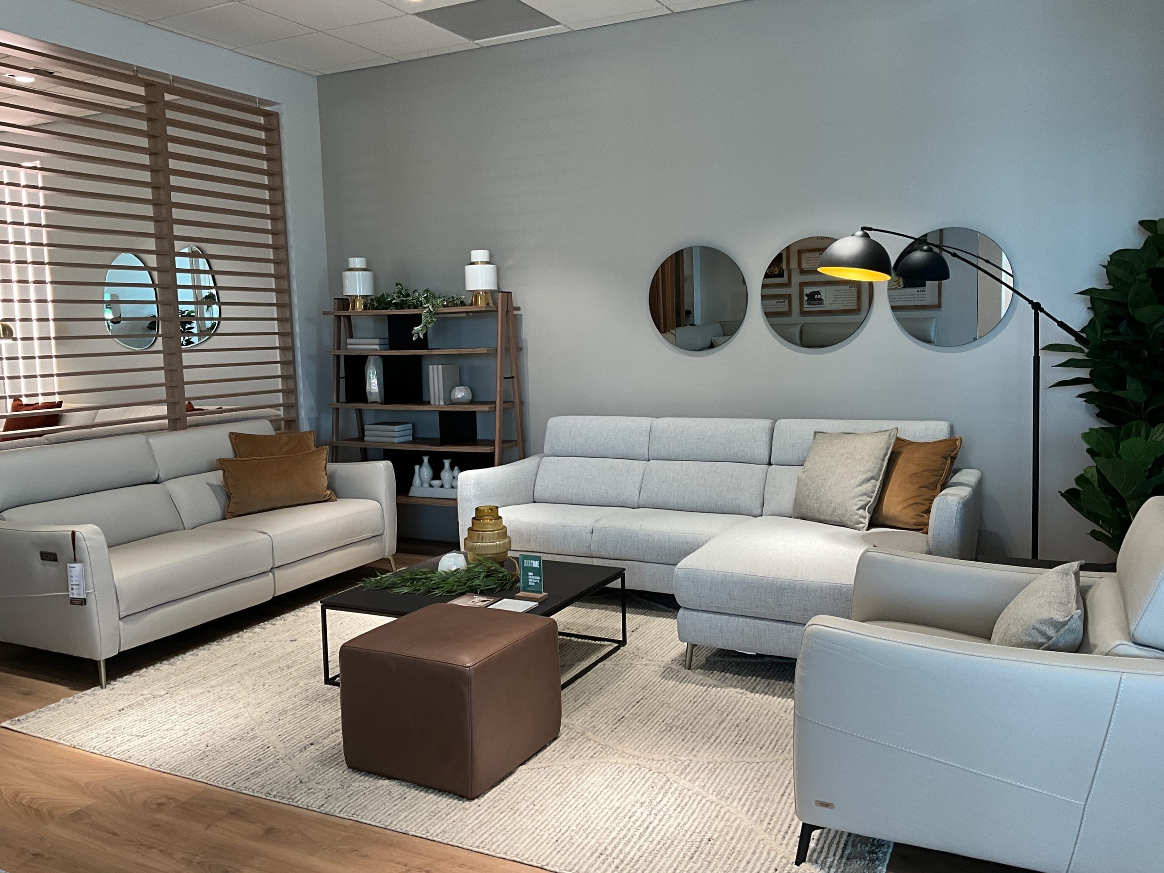 Light-gray sectional and sofa grouping beneath a trio of round mirrors and an arc floor lamp.