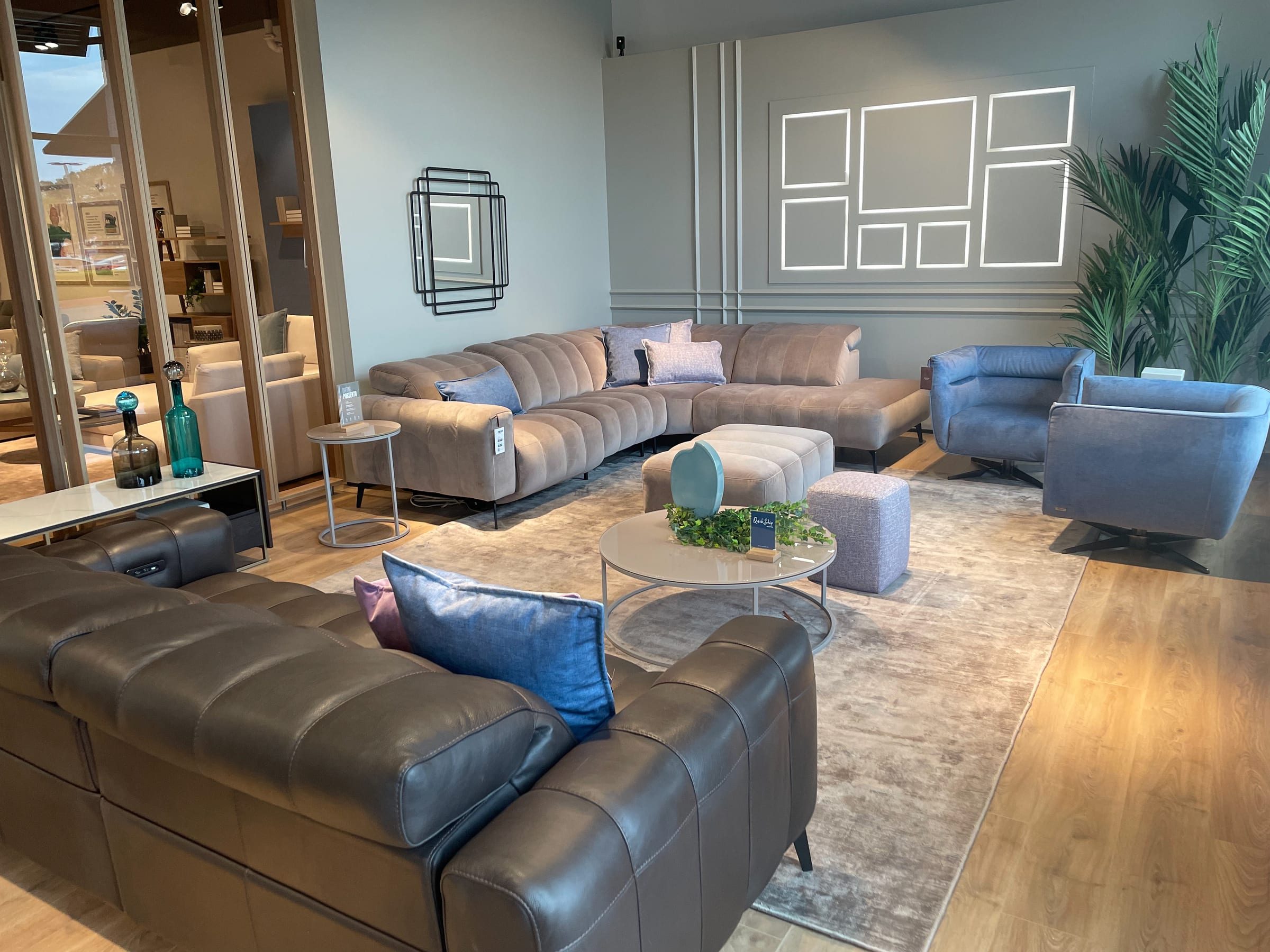 Channel-tufted sofa with blue swivel chairs, staged in front of an illuminated gallery-frame wall.